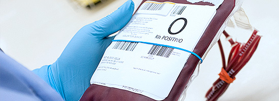 Mão com luva segurando bolsa de sangue do tipo O positivo